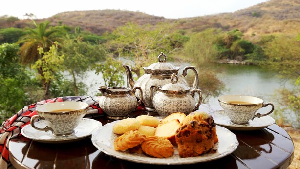 A table set with tea cups, a teapot, and pastries by a lake.