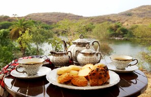 A table set with tea cups, a teapot, and pastries by a lake.