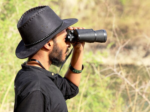 A person wearing a black hat and a black shirt, holding a camera with a long lens.