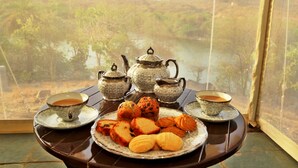 A table with tea sets, teapots, and pastries, set against a scenic view of a lake and forest.