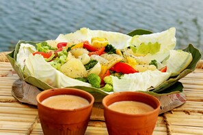 A salad with various vegetables and two small clay cups on a bamboo mat.