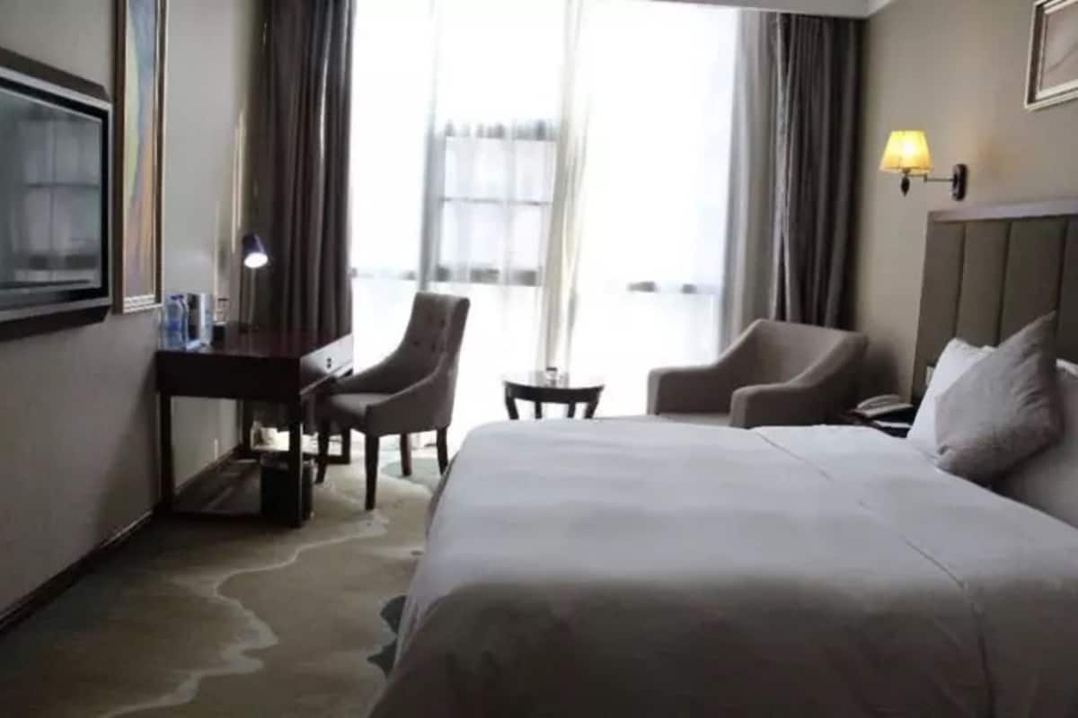 Habitació d'hotel amb un llit gran, dues butaques, un escriptori, una làmpada i vista a l'exterior.