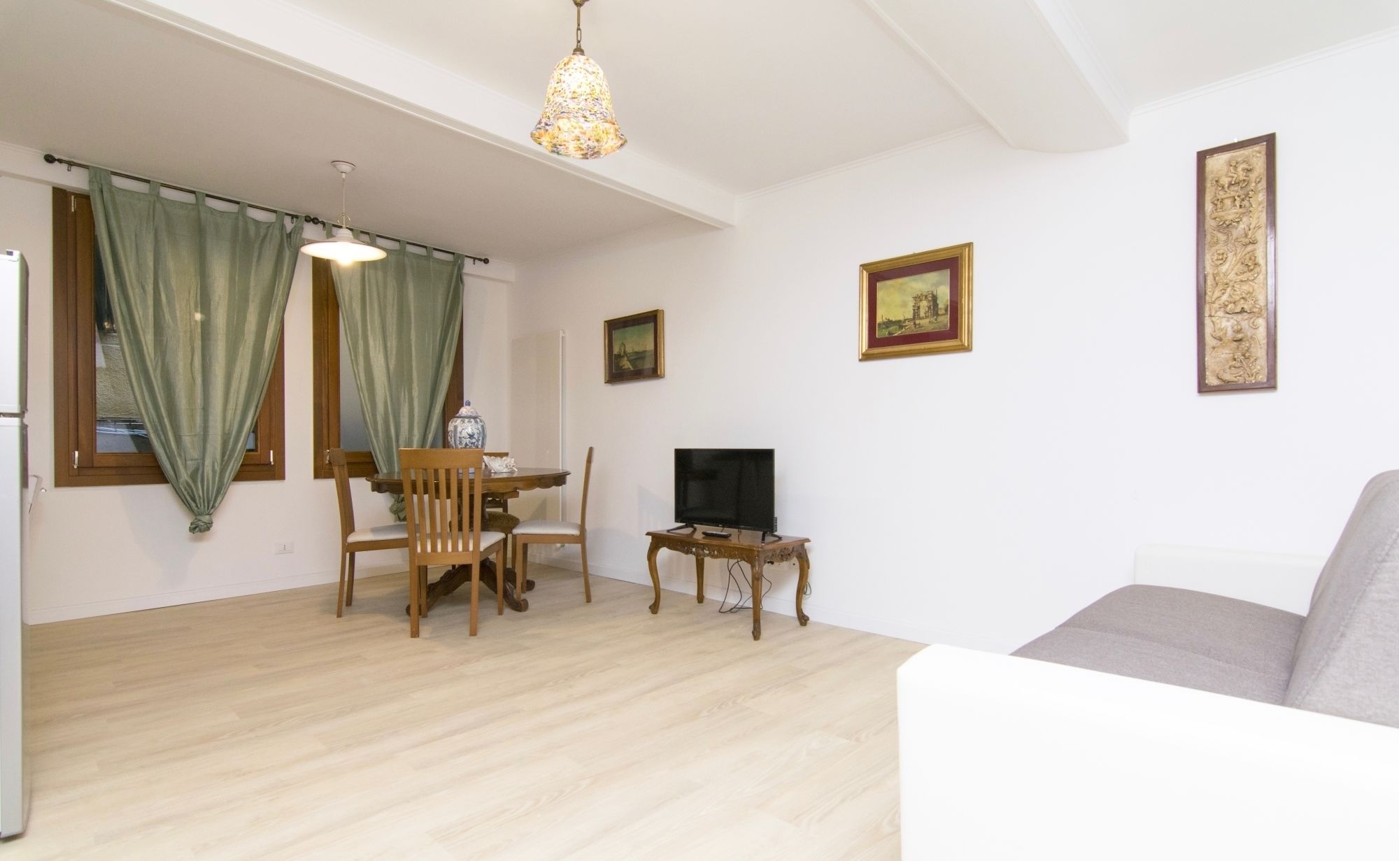 Una sala de estar con televisor, sofá, mesa de comedor con sillas y una araña.