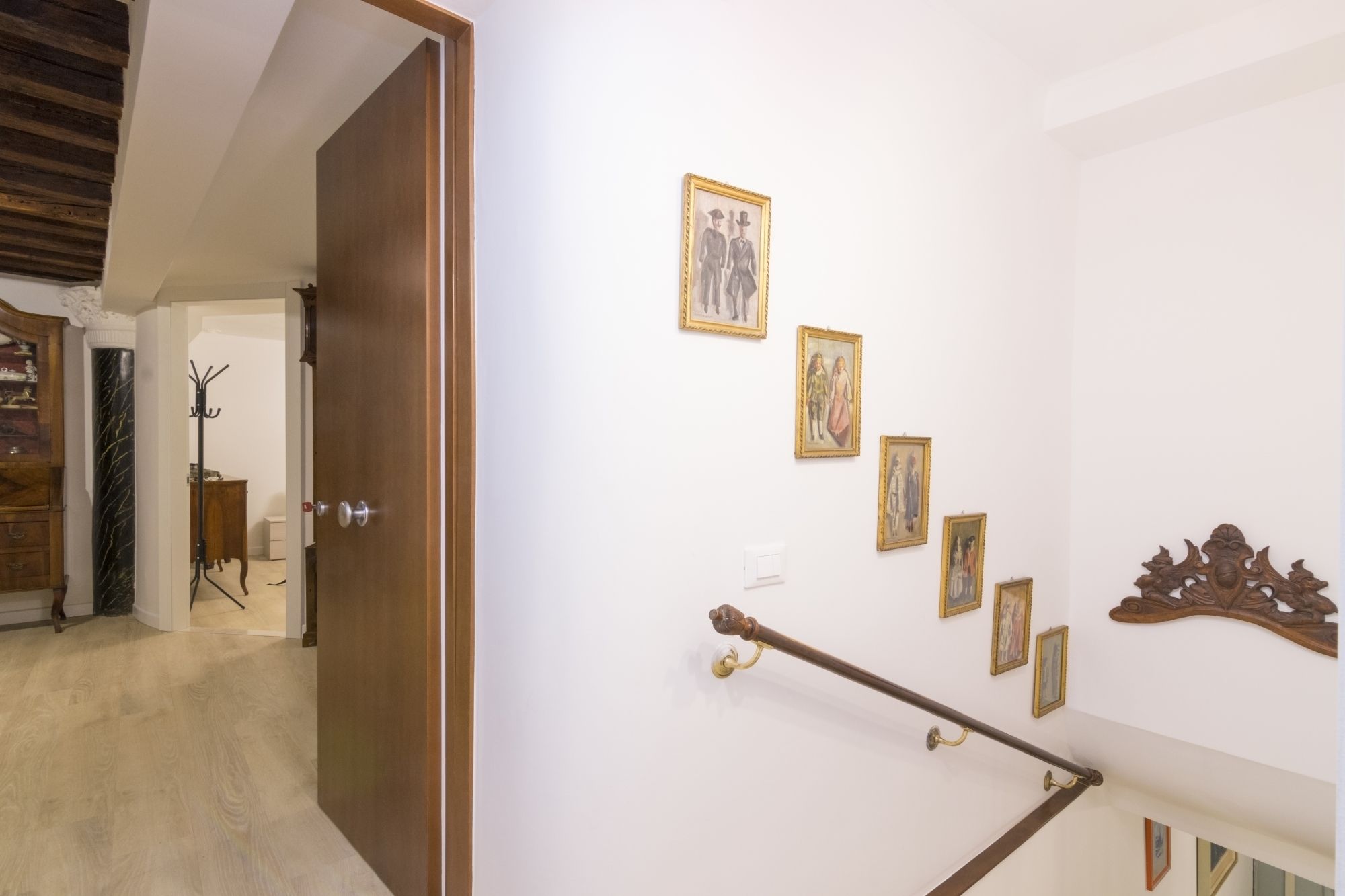 A staircase with a handrail, a wooden door, and several framed pictures on the wall.