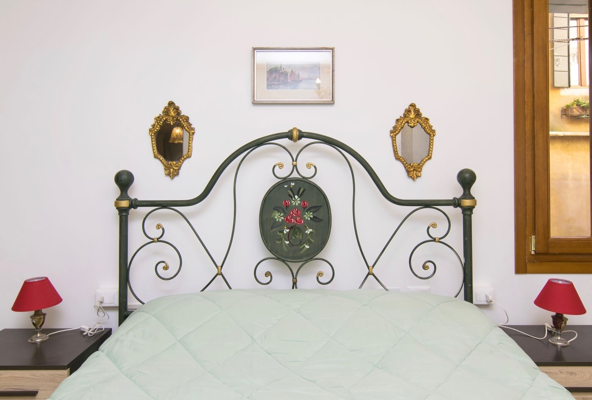Ein Bett mit einer grünen Steudecke, einem dekorativen Spiegel und einem kleinen gerahmten Bild an der Wand.