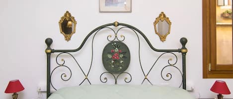 Een bed met een groene sprei, een decoratieve spiegel en een klein fotolijstje aan de muur.