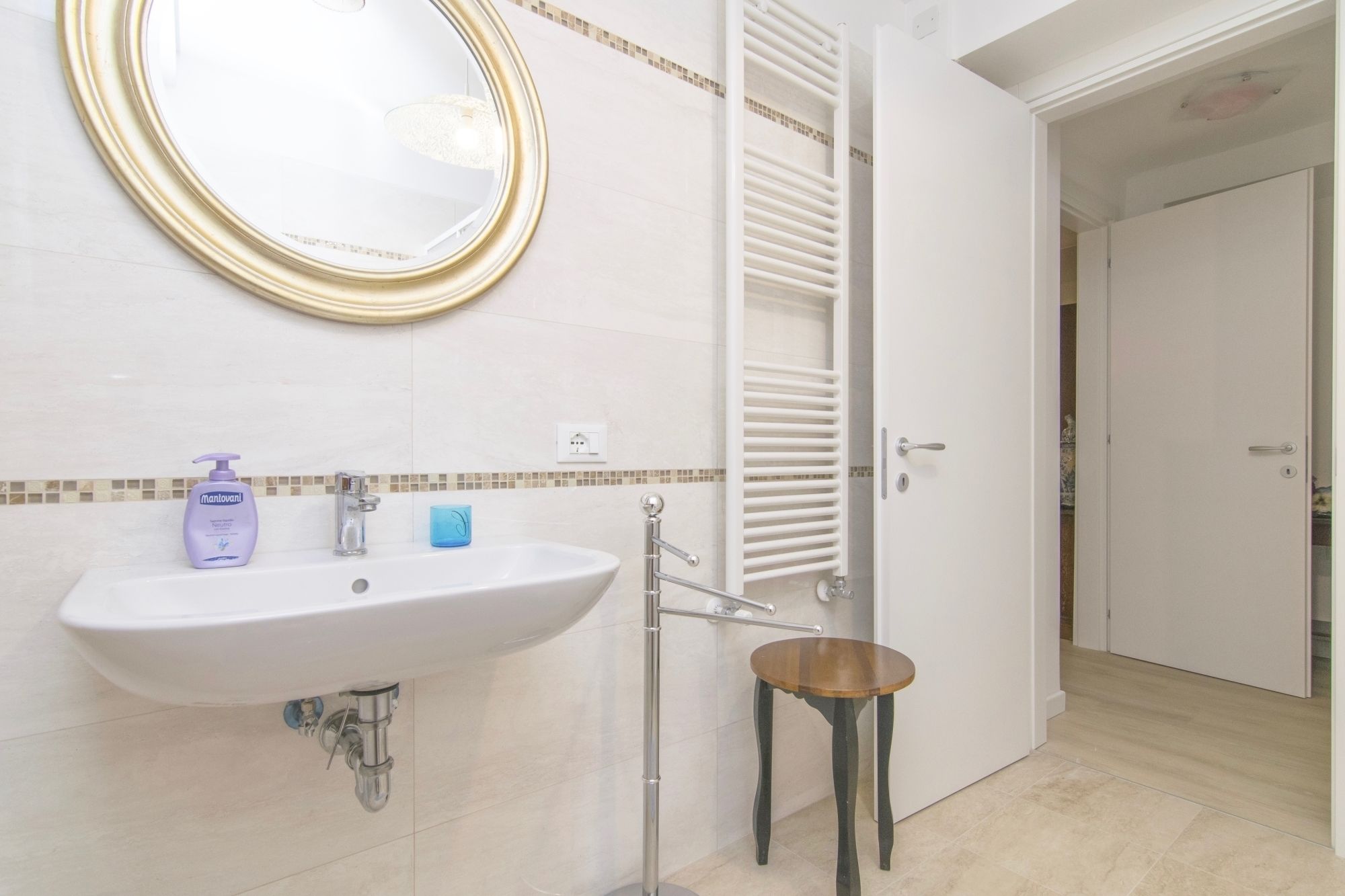 Une salle de bain avec un lavabo blanc, un miroir, un porte-serviettes et un petit tabouret en bois.