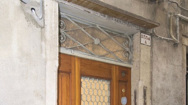 A wooden door with a glass panel and a metal plaque. - Ca' Alberto Apartments 2 (Venice)