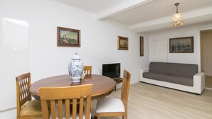A dining area with a round wooden table, chairs, a vase, and a television. There is a grey sofa and a painting on the wall. - Ca' Alberto Apartments 2 (Venice)