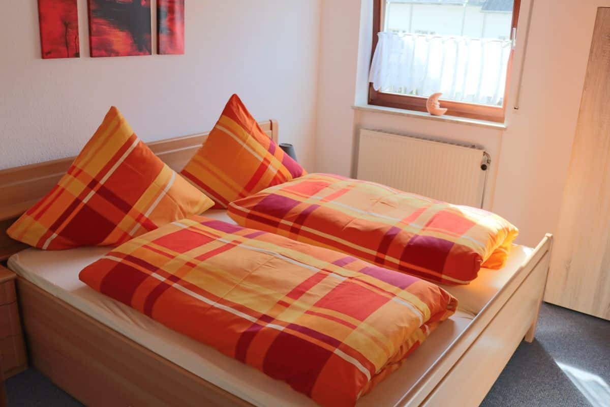 A double bed with plaid bedding in a room with a window, radiator, and artwork on the wall.