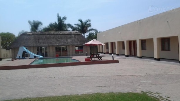 Zona de piscina con tobogán, mesa de picnic y edificio con múltiples ventanales.