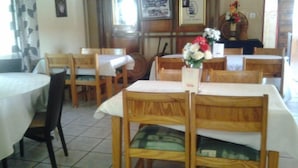Un restaurante con mesas y sillas de madera, piso de baldosas y un ventanal con cortinas.