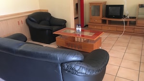 Una sala de estar con un sofá de cuero negro, una mesa de centro de vidrio, un aparador de madera y un televisor.