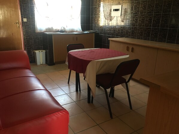 Un coin repas avec un banc rembourré de couleur rouge, une table recouverte d’une nappe rouge et un espace cuisine doté d’un pare-feu en marbre.