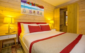 A wooden-paneled room with a bed, two bedside lamps, a painting of beach chairs, and a red headboard. - Zina Beach Resort & SPA (Abdelmalek Ramdane)
