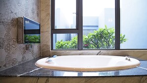A bathroom with a large bathtub, a window with a view of greenery, and a decorative wall with a geometric pattern.