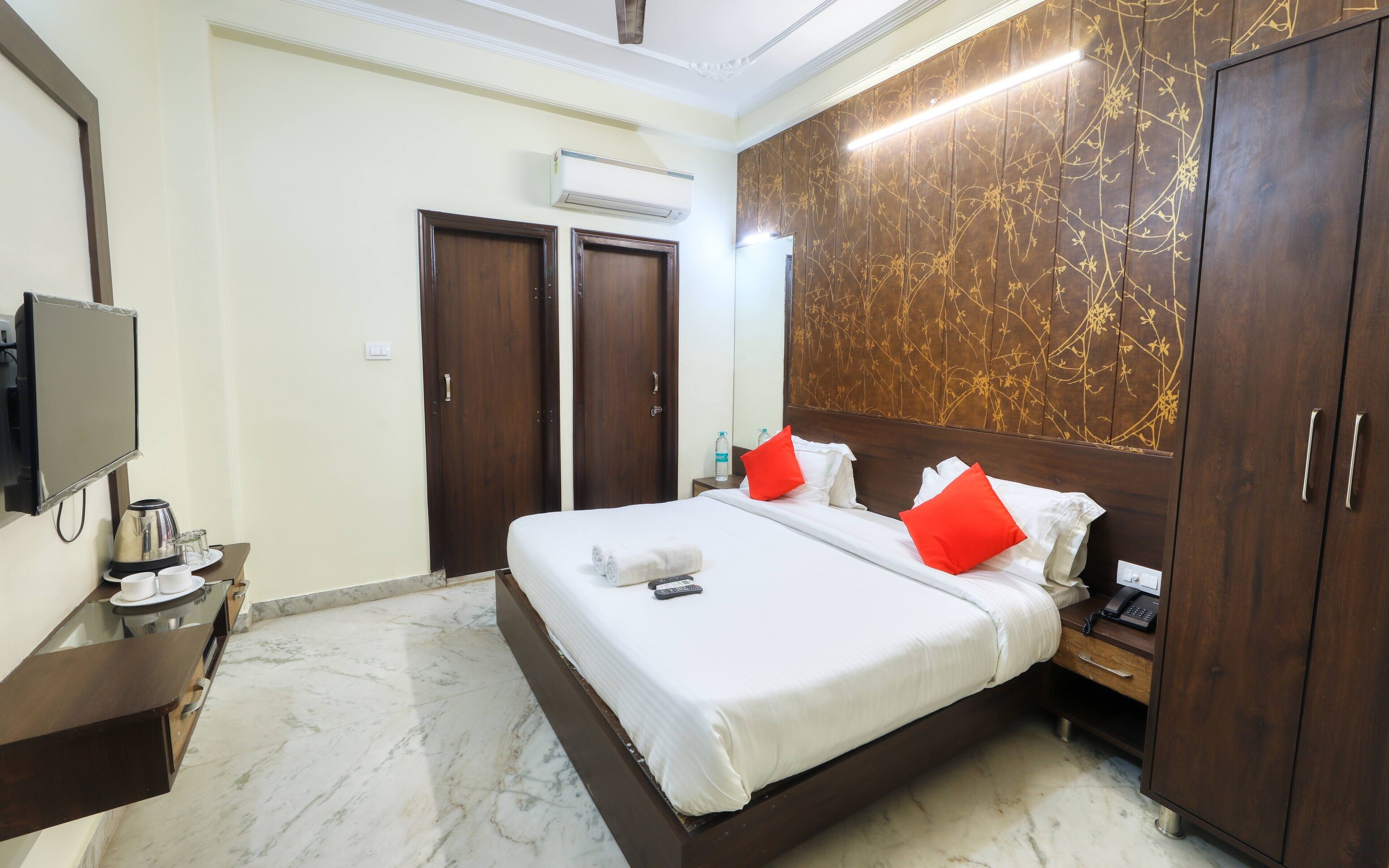 A hotel room with a large bed, a bedside table with a phone, a TV, and a minibar.