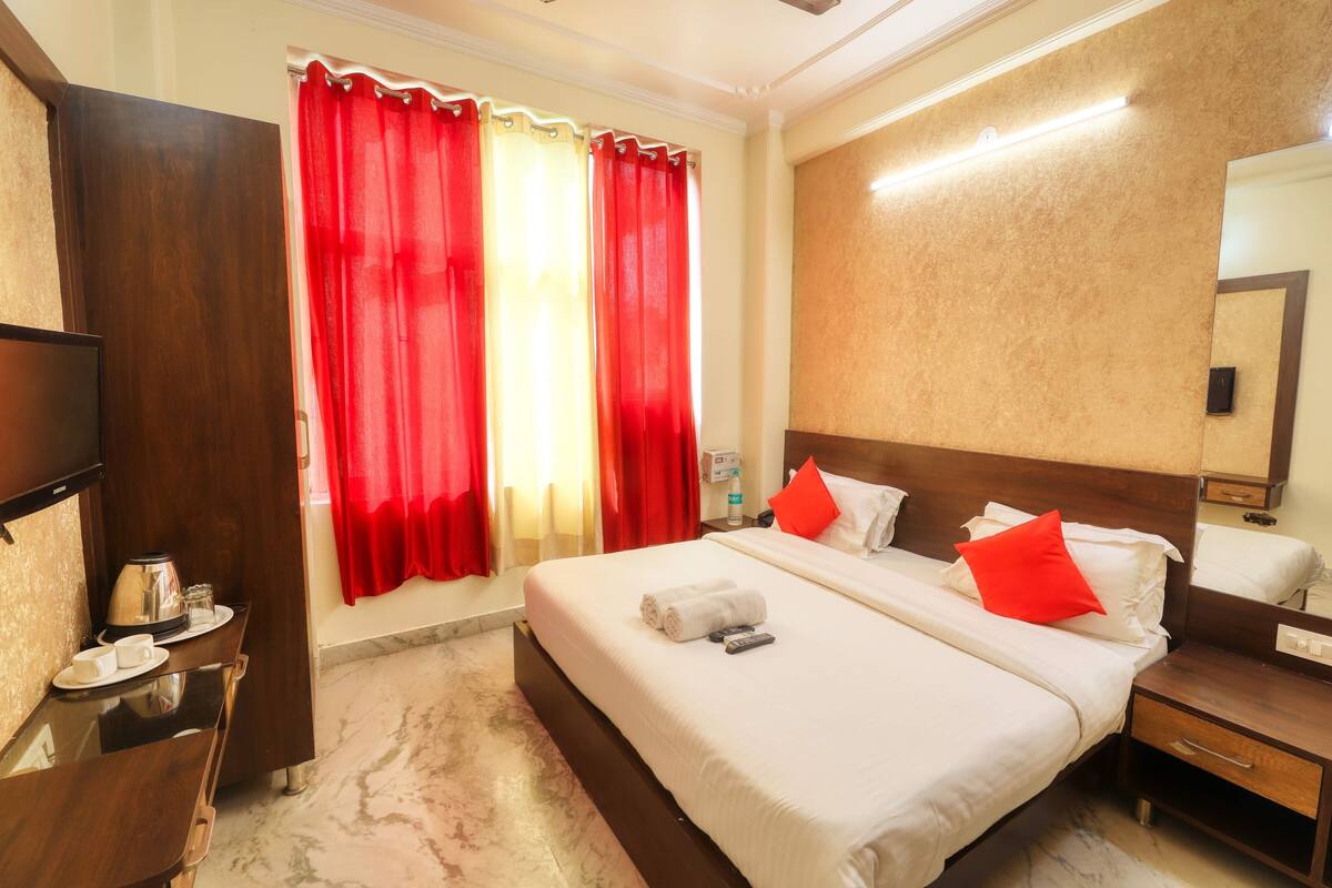 A hotel room with a bed, bedside table, TV, and a mirror.