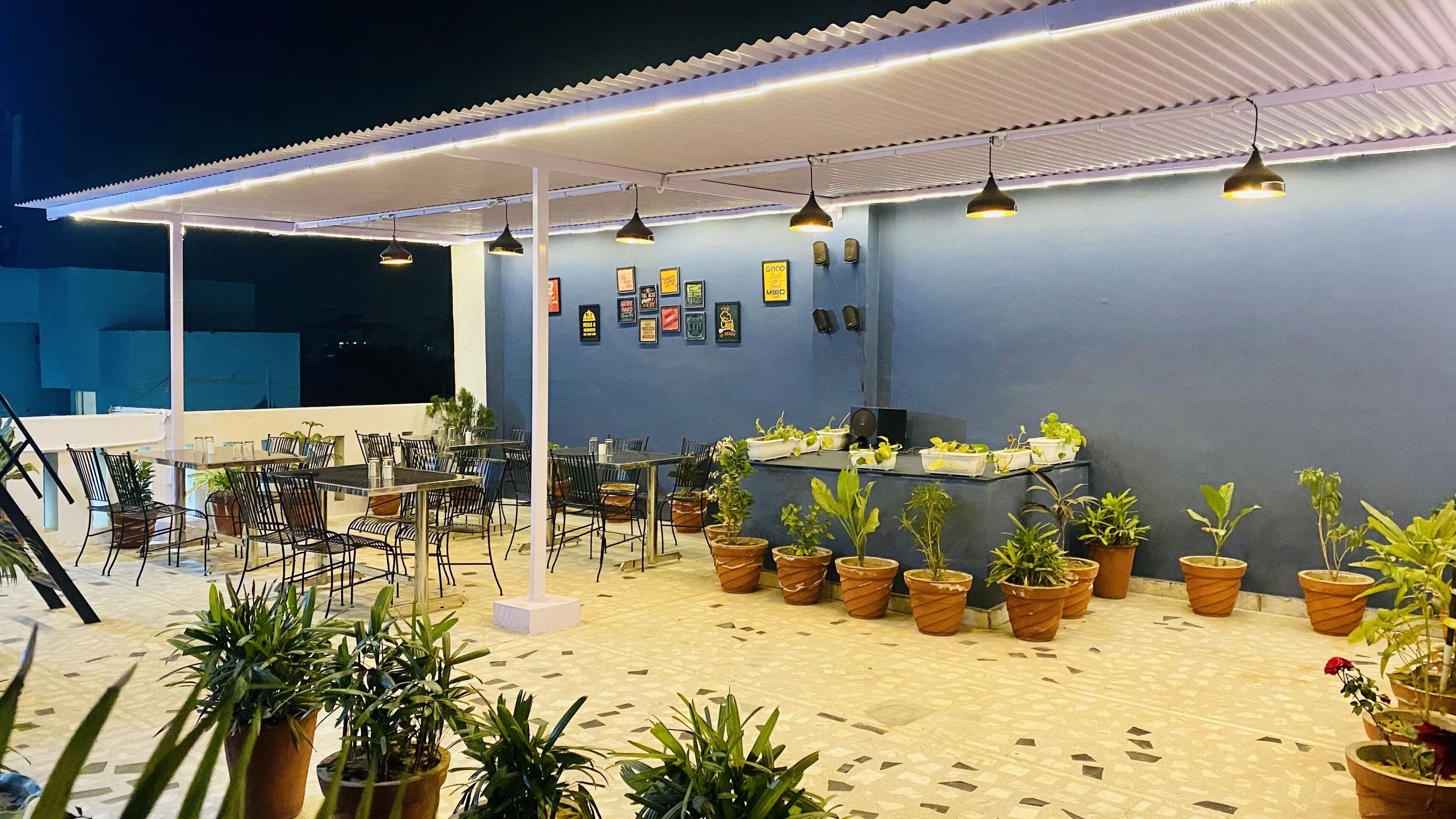 An outdoor patio area with tables and chairs, potted plants, and a covered seating area with hanging lights.