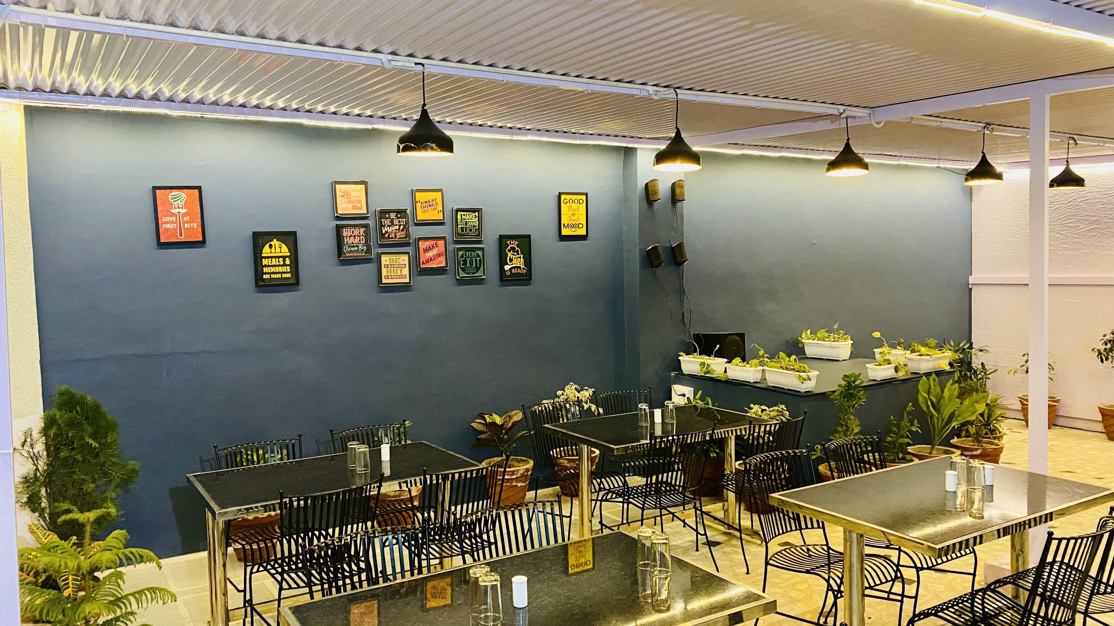 Un restaurante con mesas y sillas, carteles motivacionales en las paredes y plantas en macetas.