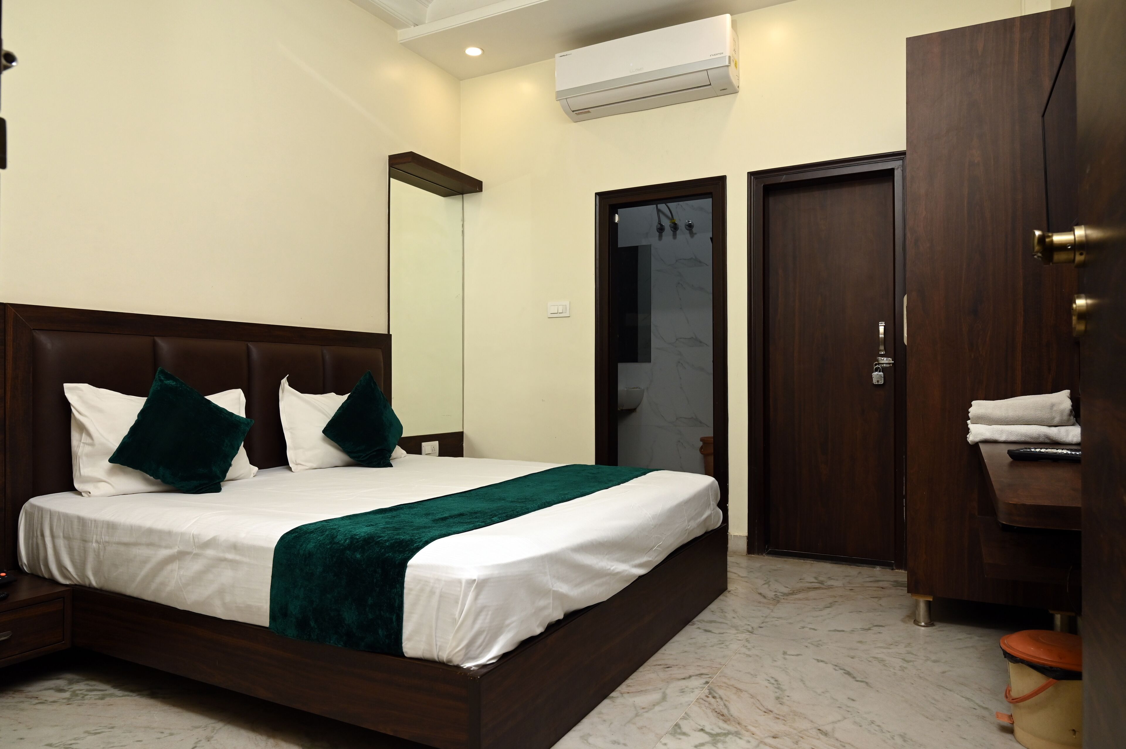 A hotel room with a large bed, a wooden headboard, a marble floor, a wardrobe, and a bathroom with a glass door.