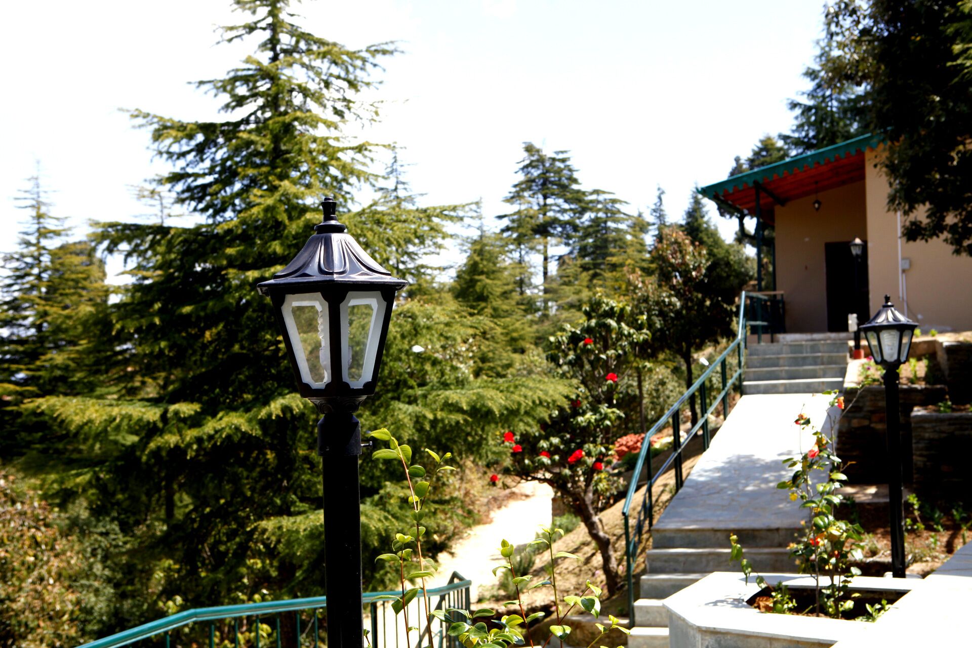 A pathway leading to a building with a red roof, surrounded by greenery and a stone wall.