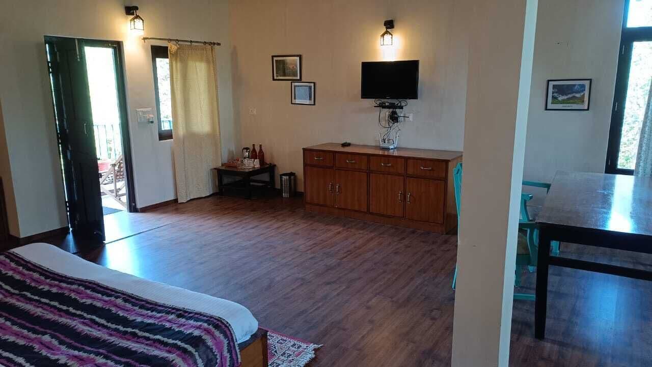 A room with wooden flooring, a bed with a patterned blanket, a wooden cabinet, a television, and a window with curtains.