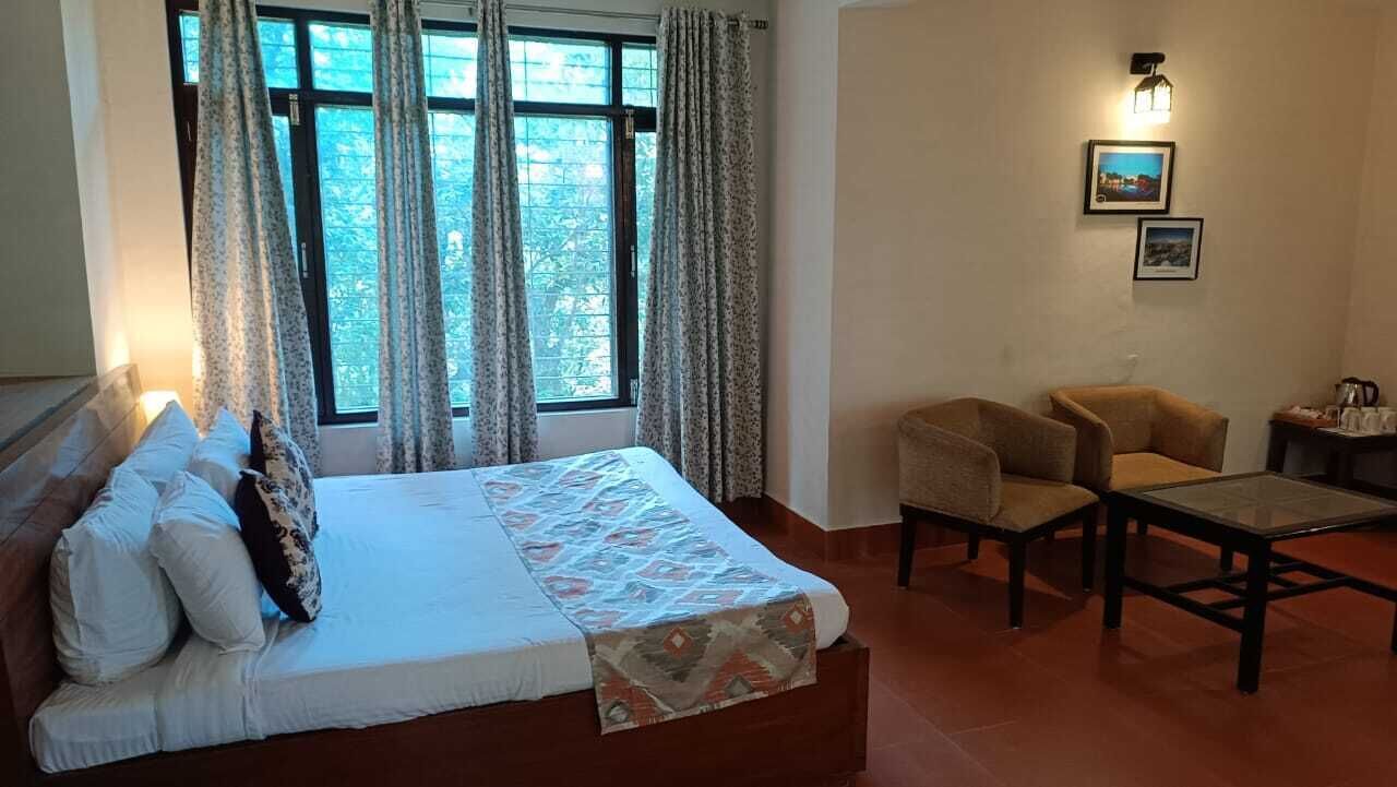 A hotel room with a bed, two chairs, a small table, and a window with curtains.