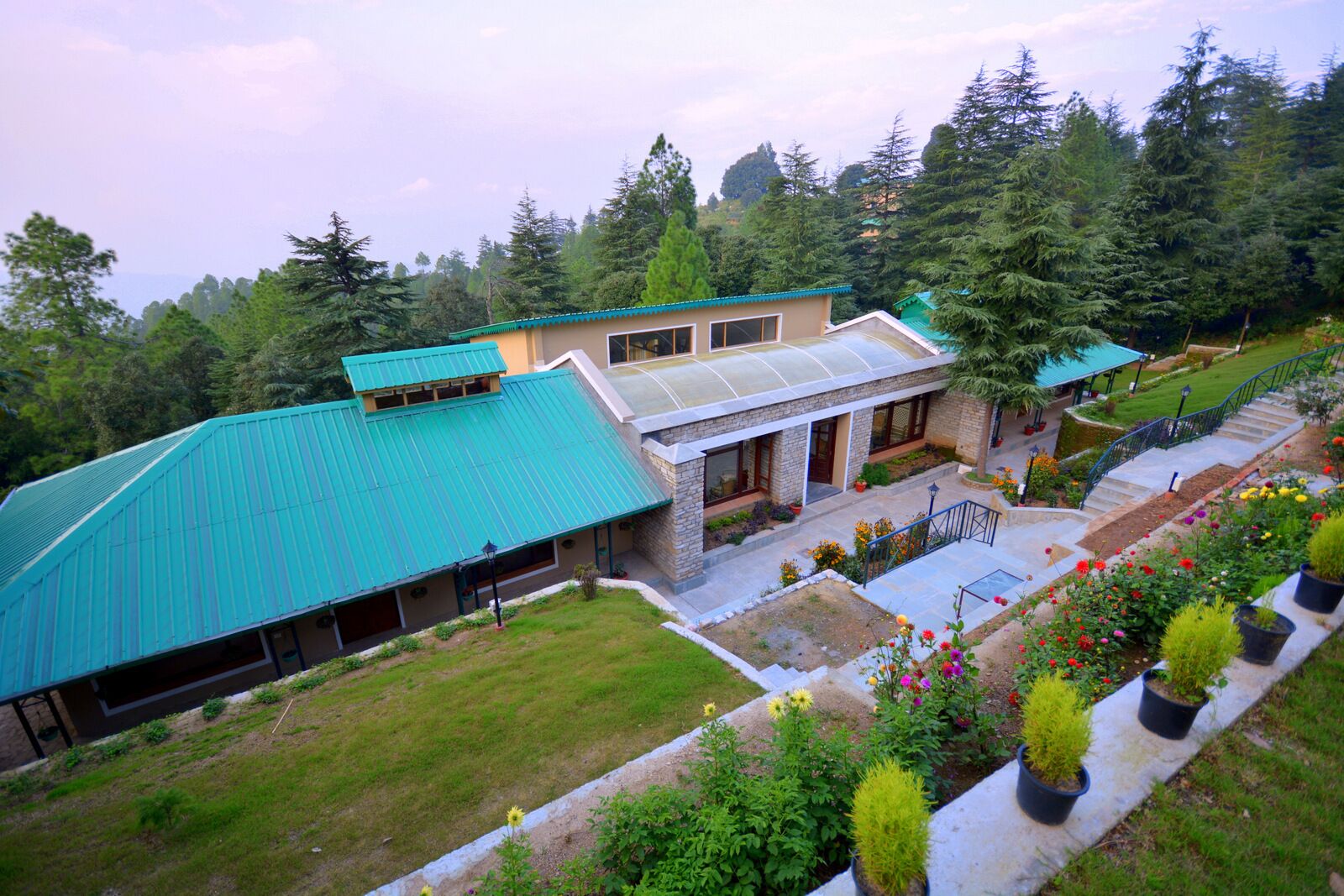 A two-story building with a green roof, surrounded by lush greenery and a garden with various plants and flowers.