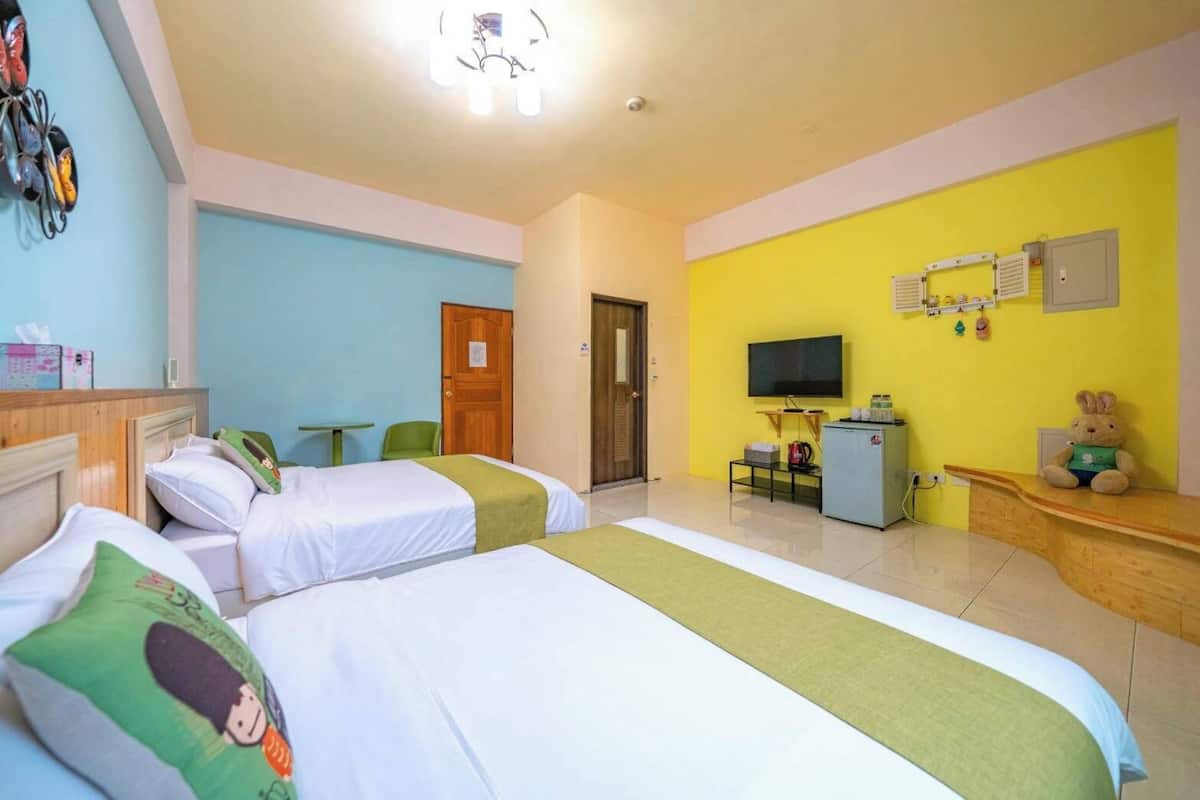 Quarto de hotel com duas camas, televisão, frigorífico e uma pequena mesa.