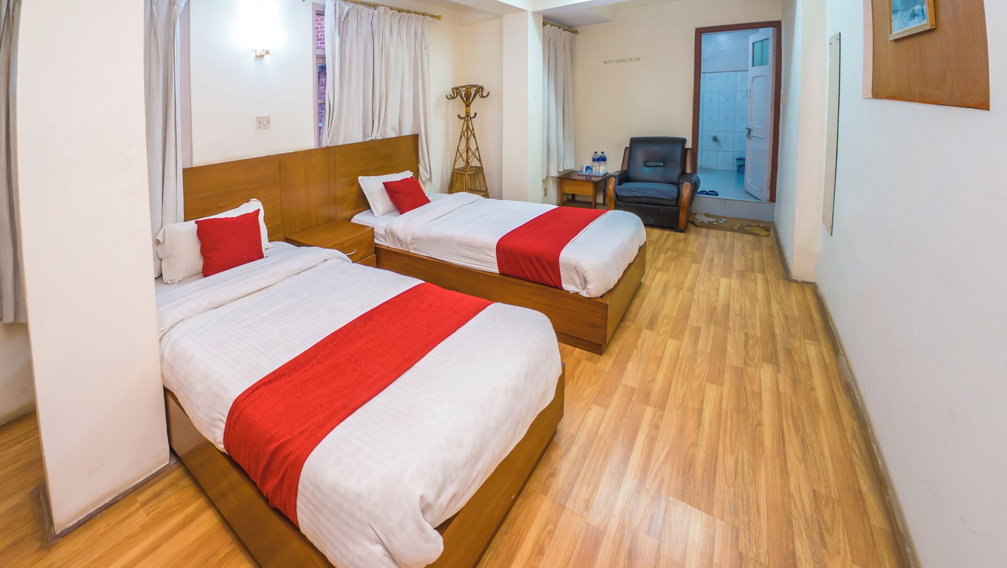A hotel room with two beds, wooden flooring, a small table with toiletries, and a chair.