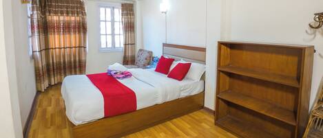 Une chambre à coucher avec un lit en bois, une literie rouge et blanche, une armoire en bois et une fenêtre avec des rideaux.