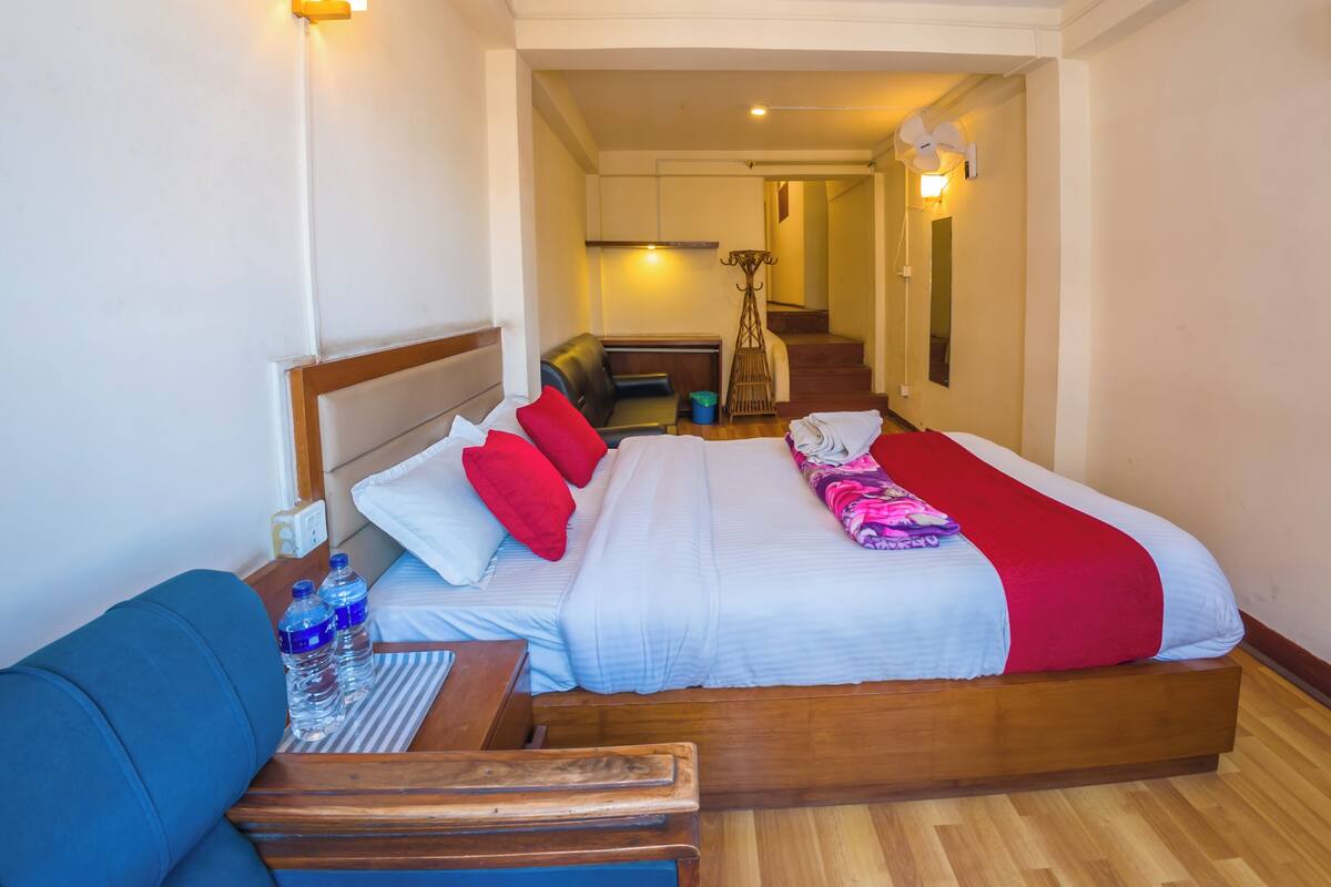 A hotel room with a bed, a wooden bench, a table with a bottle of water, and a chair.