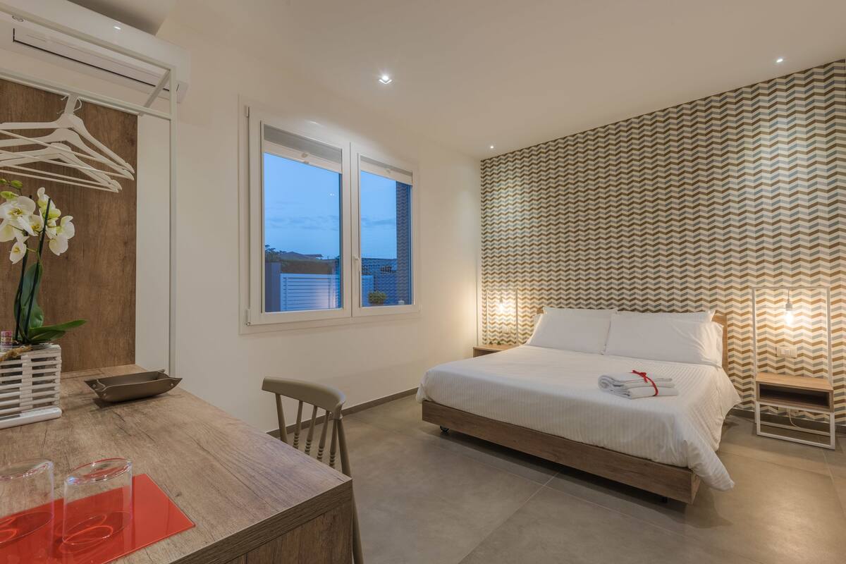 A bedroom with a bed, a desk, a chair, a window, and a patterned wall.