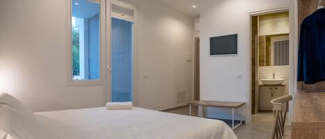 Un dormitorio moderno con una cama grande, un escritorio pequeño y un baño visible a través de una puerta abierta.