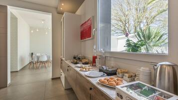 Una cocina moderna con barra para desayunos, una zona de comedor con sillas blancas y vistas a árboles.