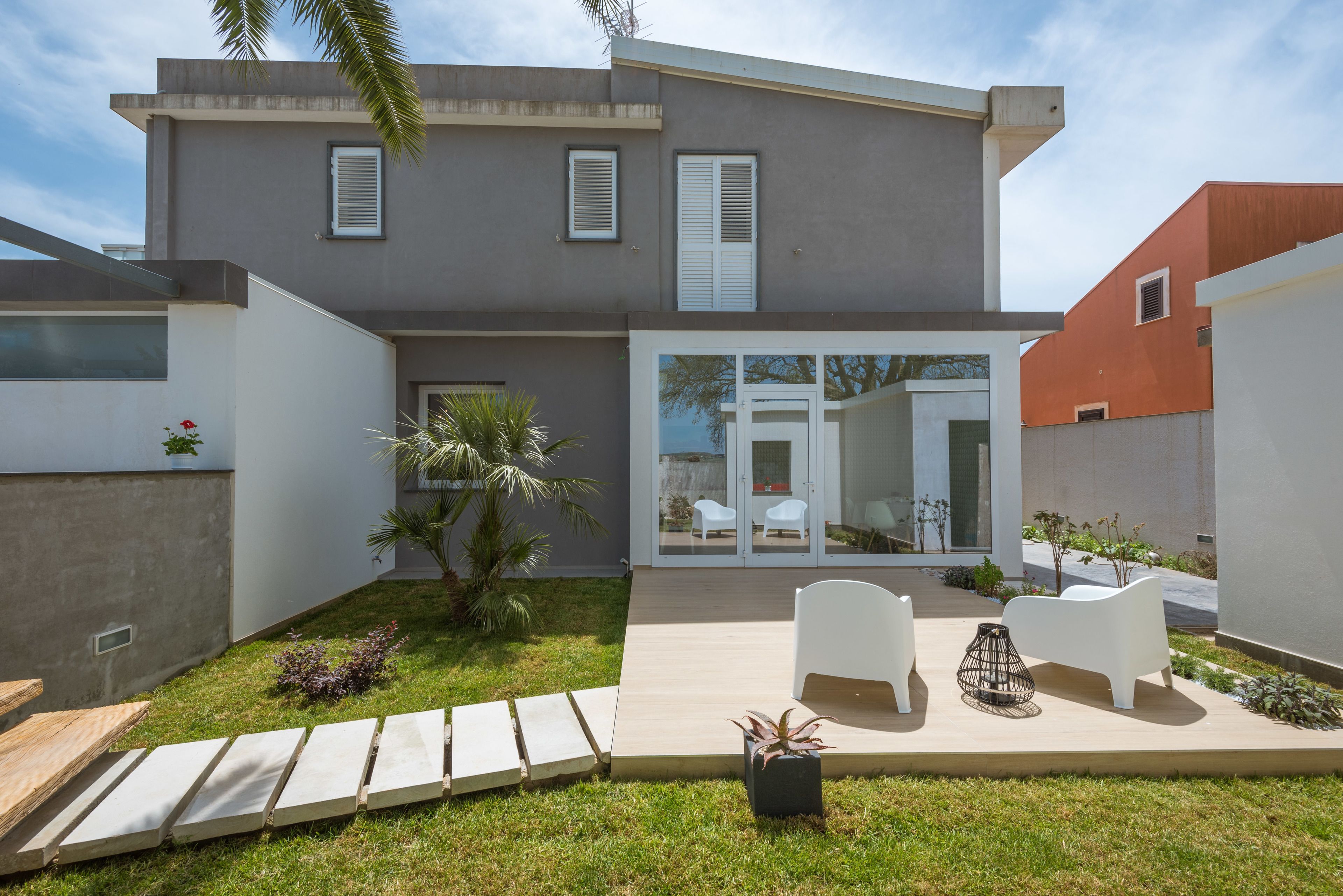 Una casa moderna de dos pisos con un patio, mobiliario exterior blanco y un pequeño jardín.