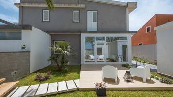 Una casa moderna de dos pisos con un patio, mobiliario exterior blanco y un pequeño jardín.