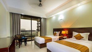 A hotel room with two beds, a desk, a chair, and a large window with a city view.