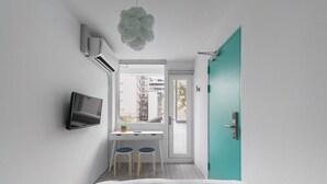 A modern bedroom with a bed, a desk with two chairs, a TV, and a teal door. - TG Hostel (Taichung)