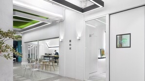 A modern office space with white walls, green ceiling accents, and a glass door leading to another room. - TG Hostel (Taichung)