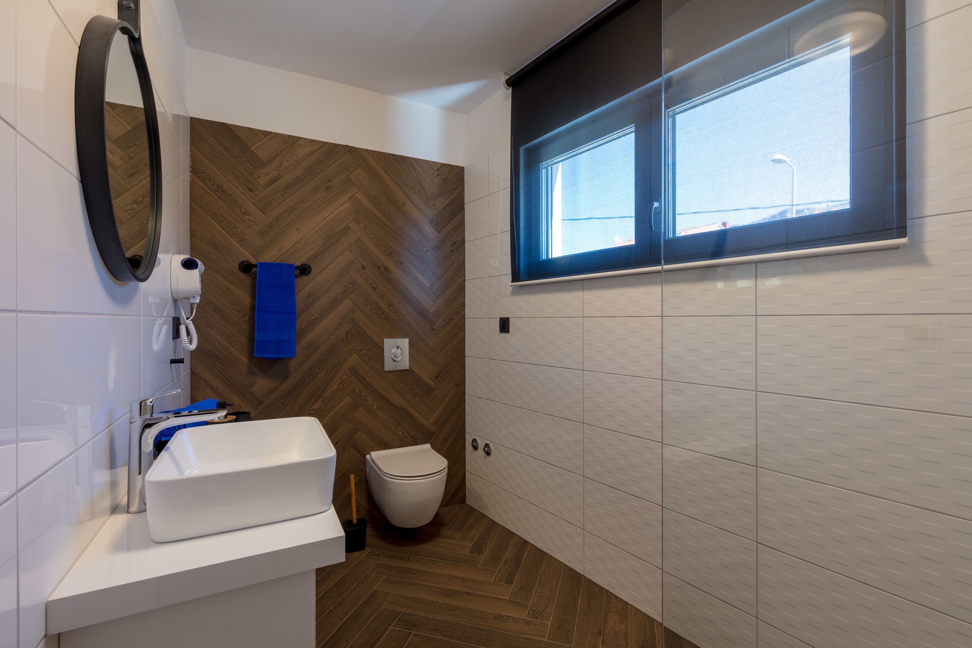Een moderne badkamer met een wit wastafel, toilet, spiegel en raam.