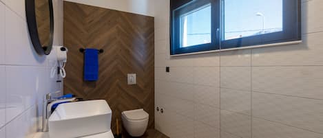 Un baño moderno con un lavamanos blanco, un inodoro, un espejo y una ventana.