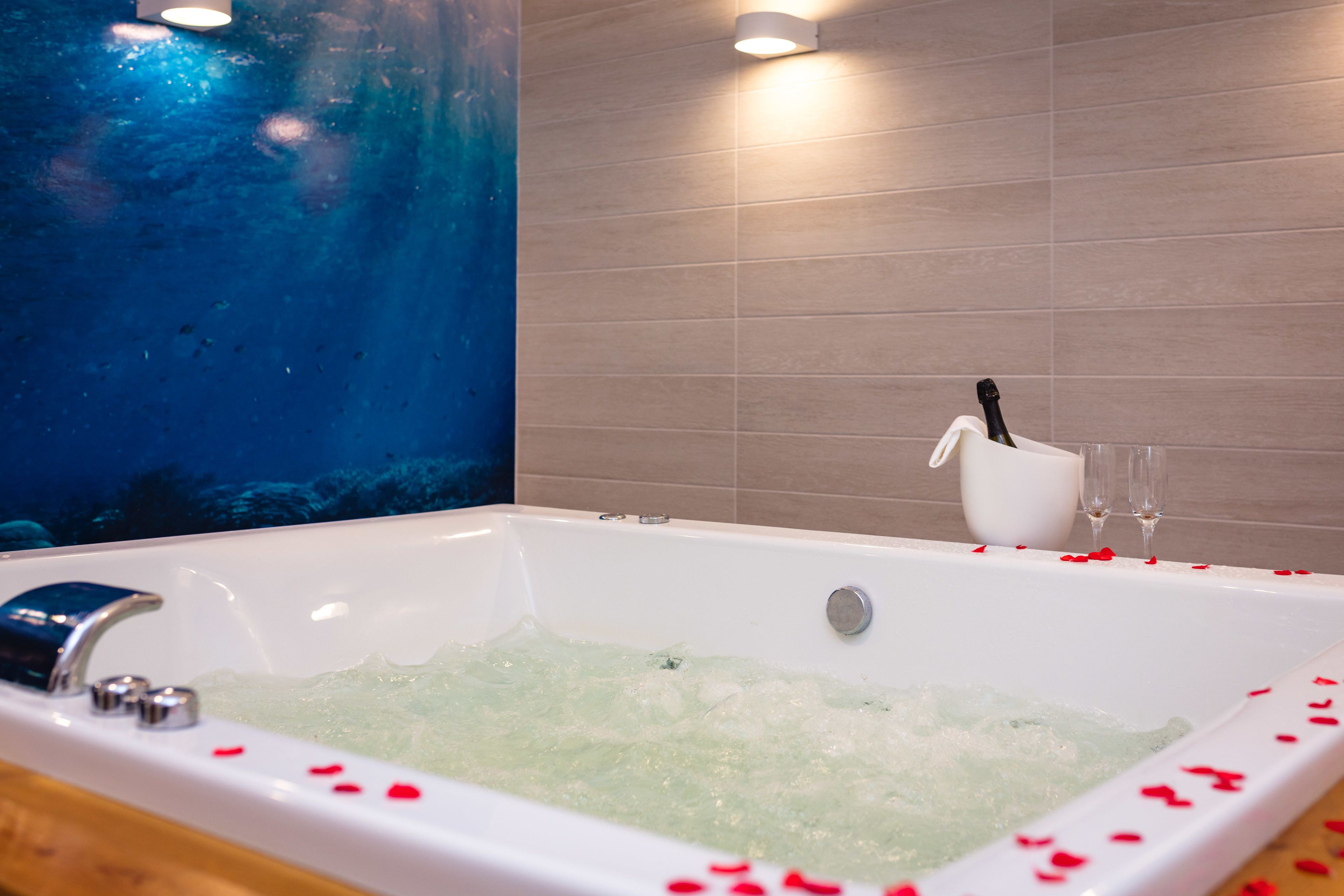 A bathtub with rose petals, a white cup, and two glasses.