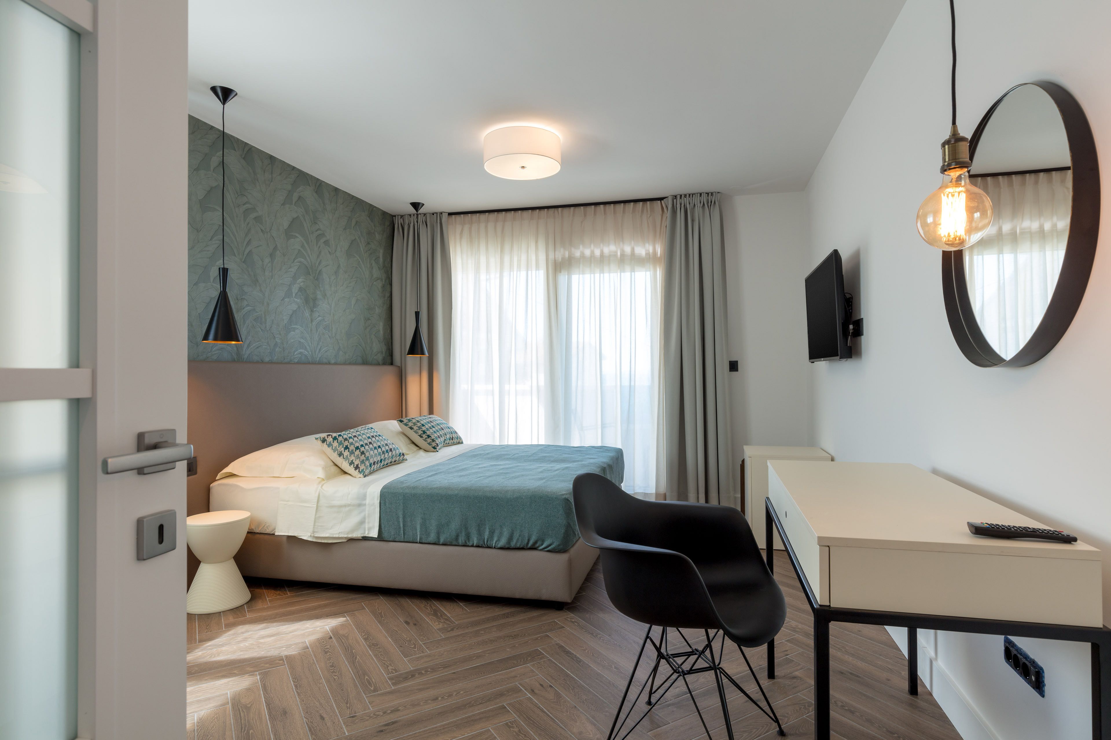 A modern bedroom with a bed, bedside table, chair, and a desk with a mirror.
