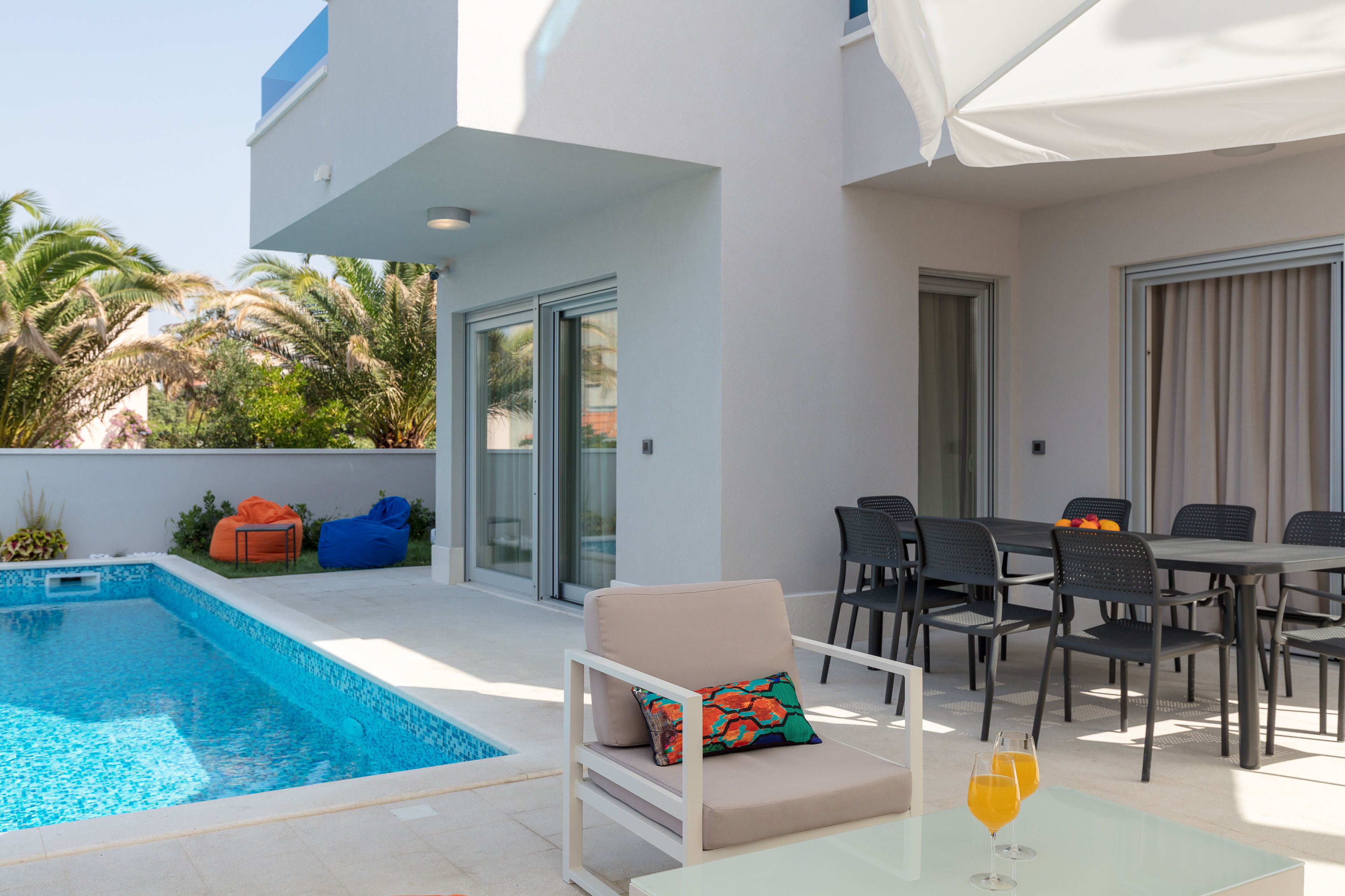 Area piscina moderna all'aperto con una poltrona prendisole, un tavolo da pranzo con sedie e un patio con vetrate.