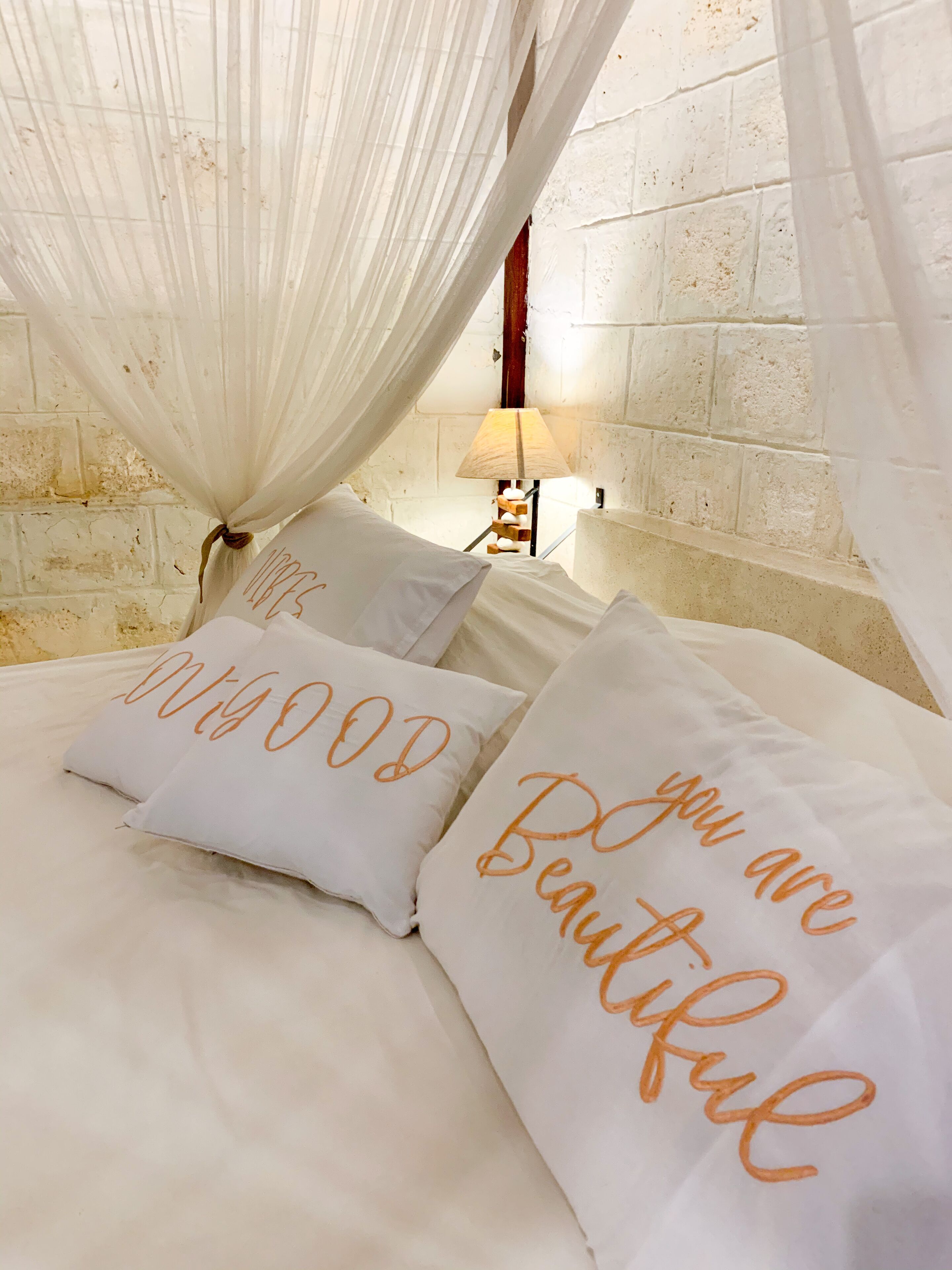 Un lit avec une literie blanche et deux oreillers ornés du texte « tu es magnifique » en orange.