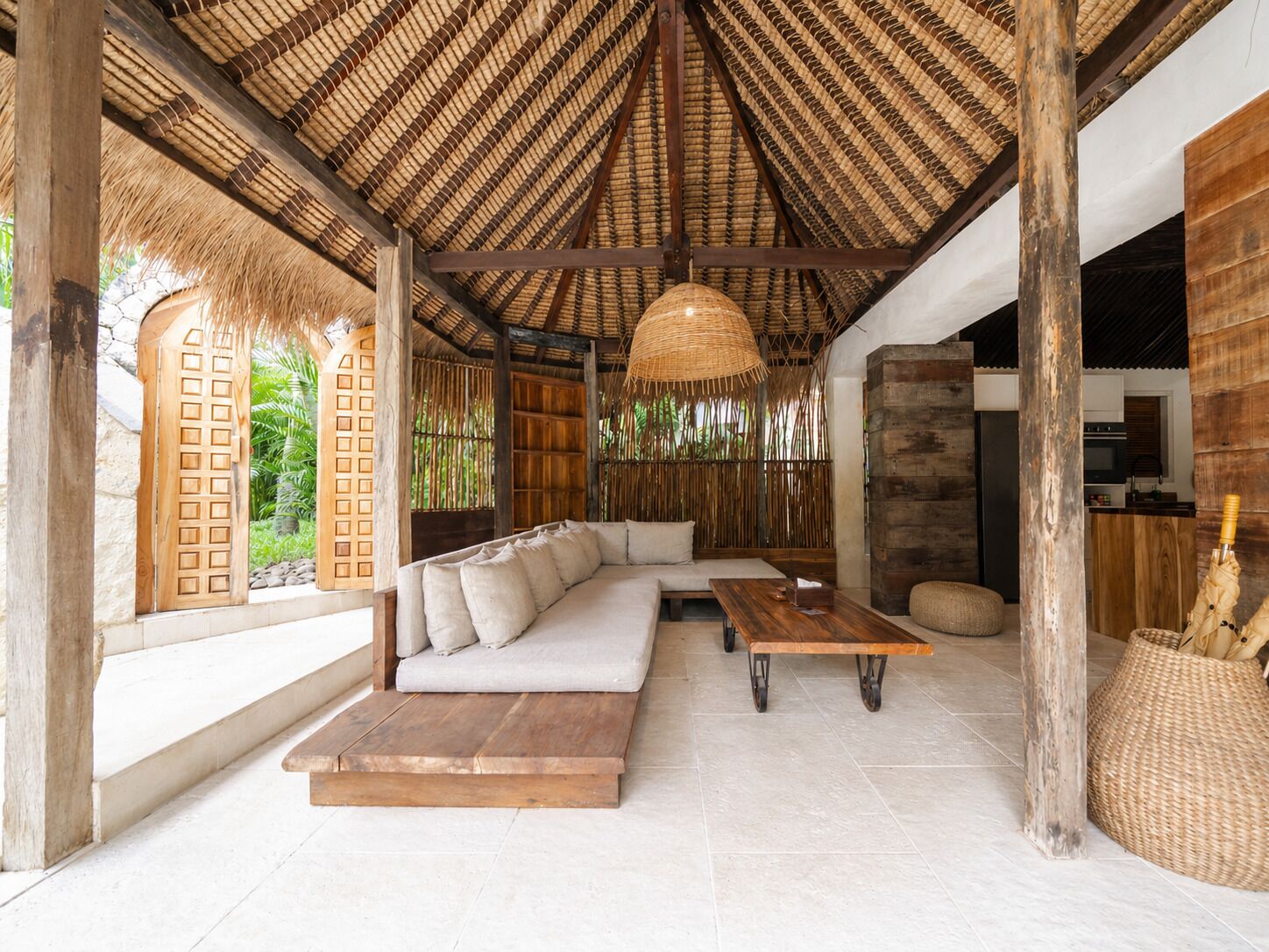 A spacious room with a thatched roof, a large sofa, a wooden table, and a woven basket.