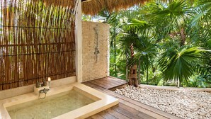 A spa area with a hot tub, bamboo walls, a brick wall, and a view of lush greenery. - La Cabane Bali (Jimbaran)