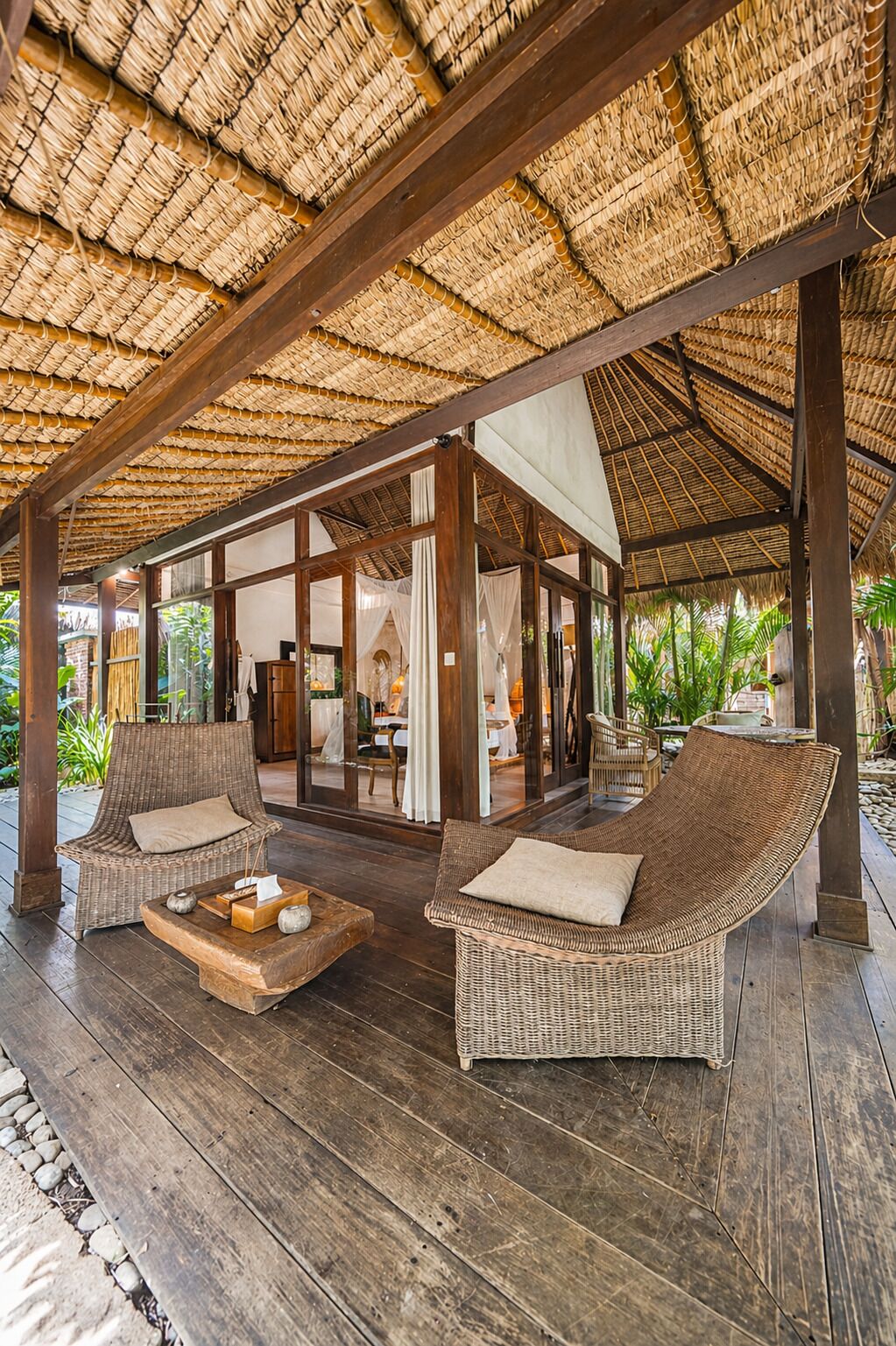 An open-air lounge with wicker furniture, a wooden floor, and a thatched roof.